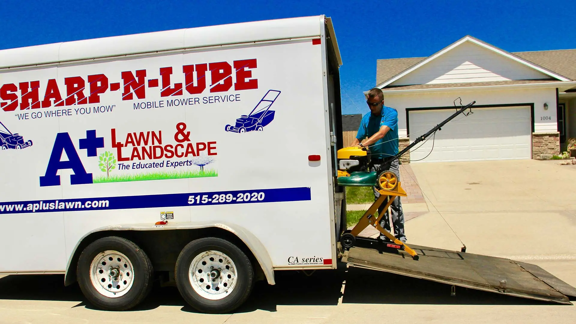 Our sharp-n-lube trailer open with a landscaper at work in front of a home in Des Moines. IA.