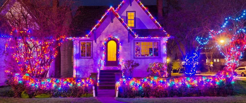 Colorful holiday lights on a house, trees, and shrubs in Des Moines, IA.
