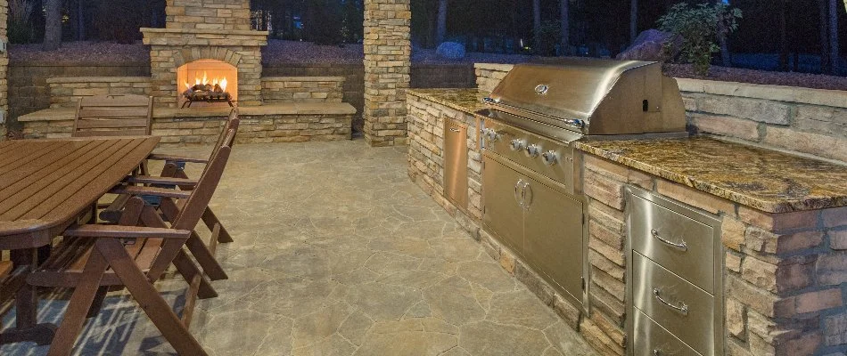 Dining furniture beside an outdoor kitchen and outdoor fireplace in Des Moines, IA.