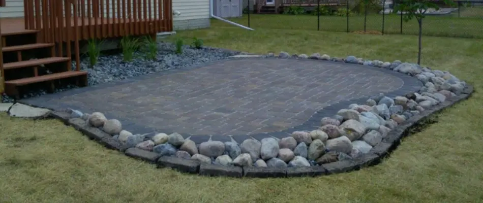 Paver patio in Des Moines, IA, with decorative stones by a lawn.