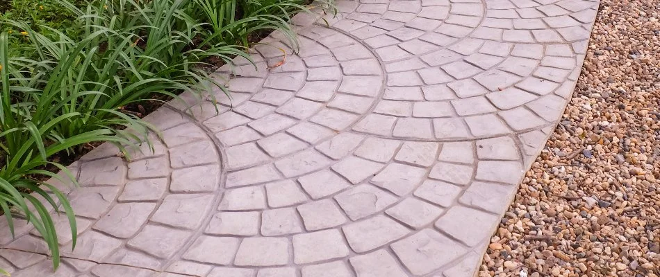 Stamped concrete pathway in Des Moines, IA, with plants and decorative rocks.