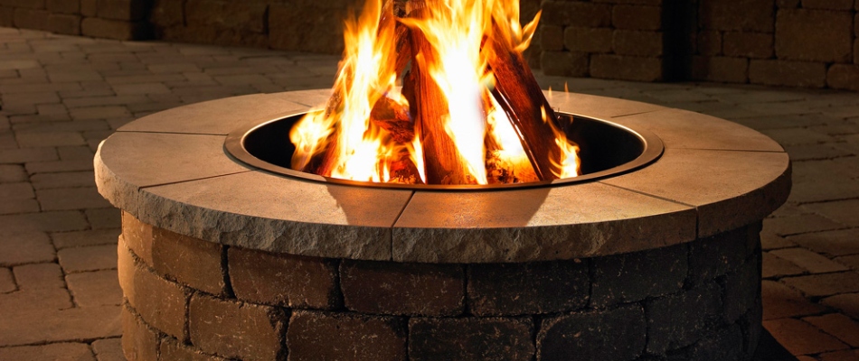 Custom stone built fire pit with flames going in West Des Moines, IA.
